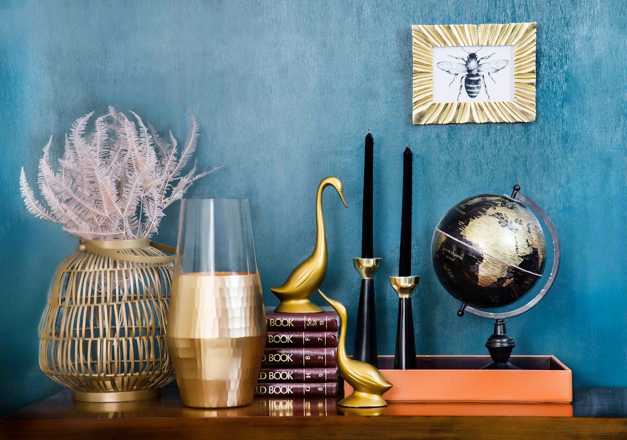 gallery-3 Stylish home decor arrangement including a globe, books, candles, and vases on a blue backdrop.