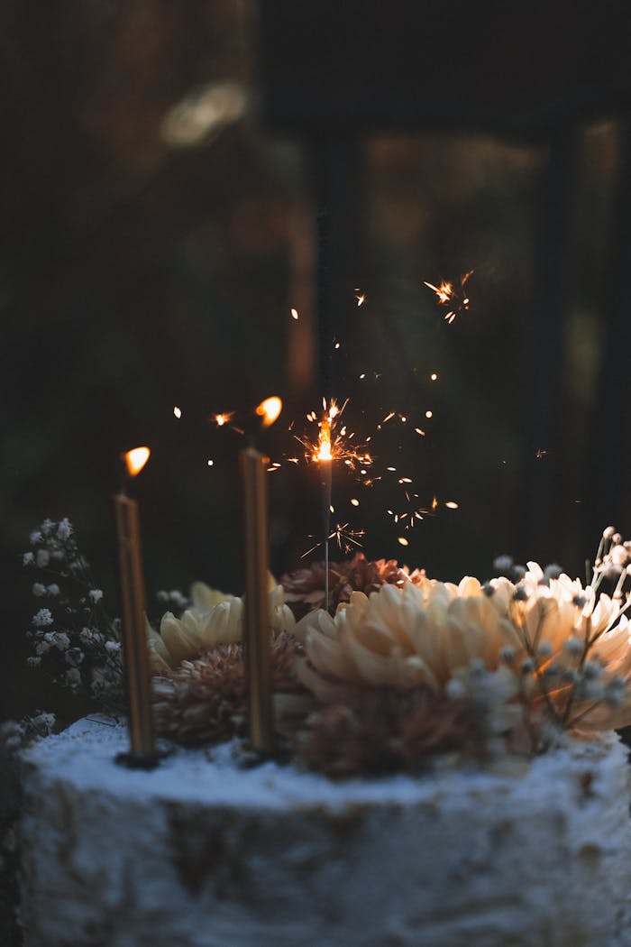 ours-journey Charming rustic birthday cake adorned with sparklers and floral decorations, captured in warm lighting.