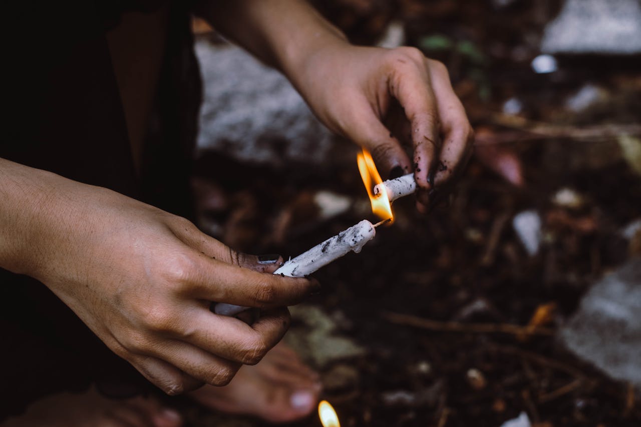 gallery-5 A person lighting white candles outdoors, focusing on hands and flame against a natural background.