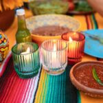 A colorful Mexican-themed table setting featuring candles, sauces, and decorative elements.
