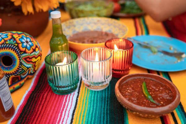 A colorful Mexican-themed table setting featuring candles, sauces, and decorative elements.