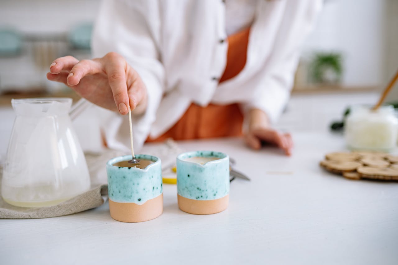 gallery-2 Close-up of hands making handmade candles using soy wax in decorative containers.