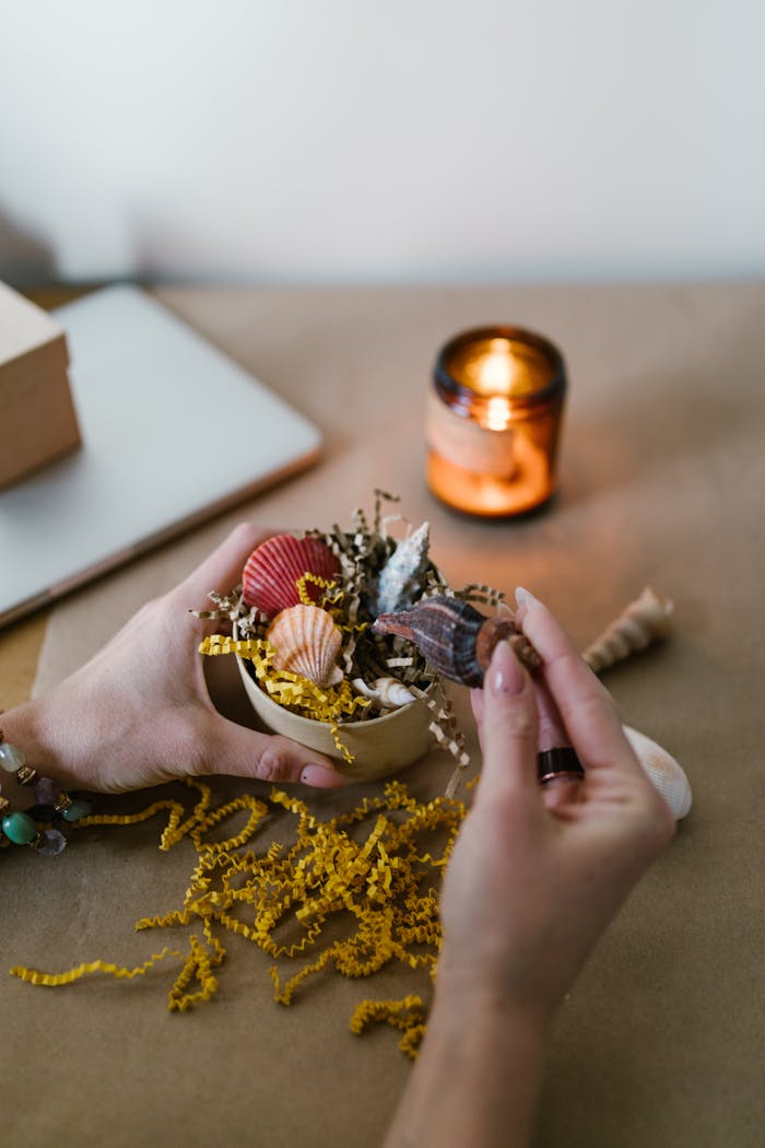 about-img Close-up of hands creating a candle with seashells and natural elements.