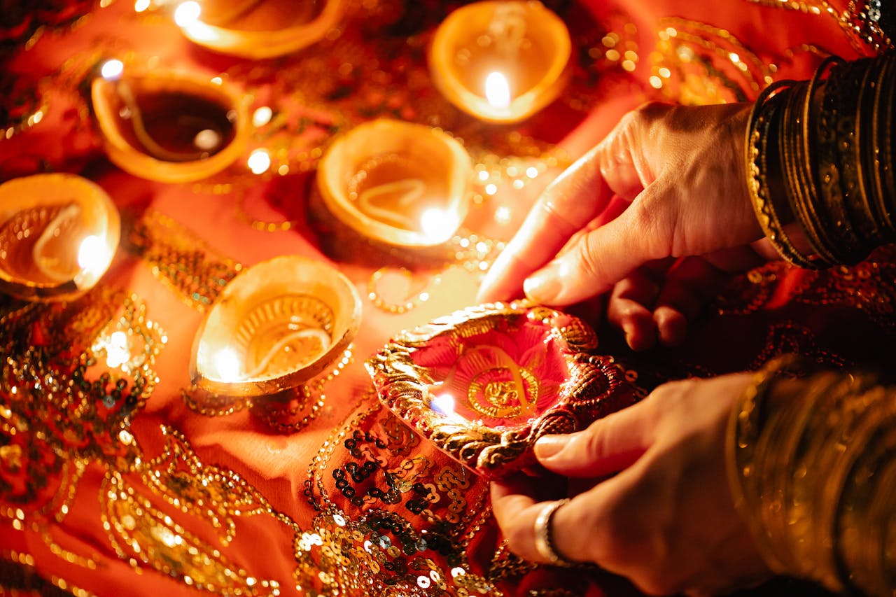 hero-img-01 Close-up of hands lighting decorative oil lamps for Diwali celebration, creating a warm festive ambiance.